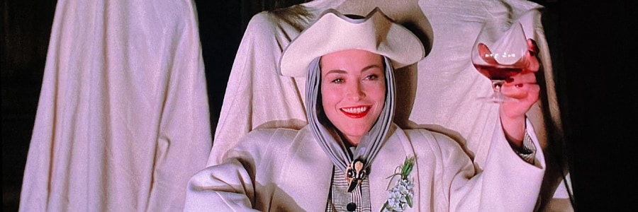 Lady Sylvia Marsh in a white suit holding a glass of red wine and laughing.