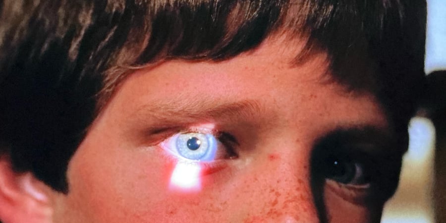 A light in a boy's eye as he looks through a keyhole.