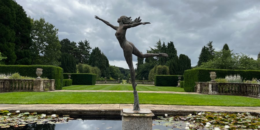 A statue of a woman in a pond at a stately home.